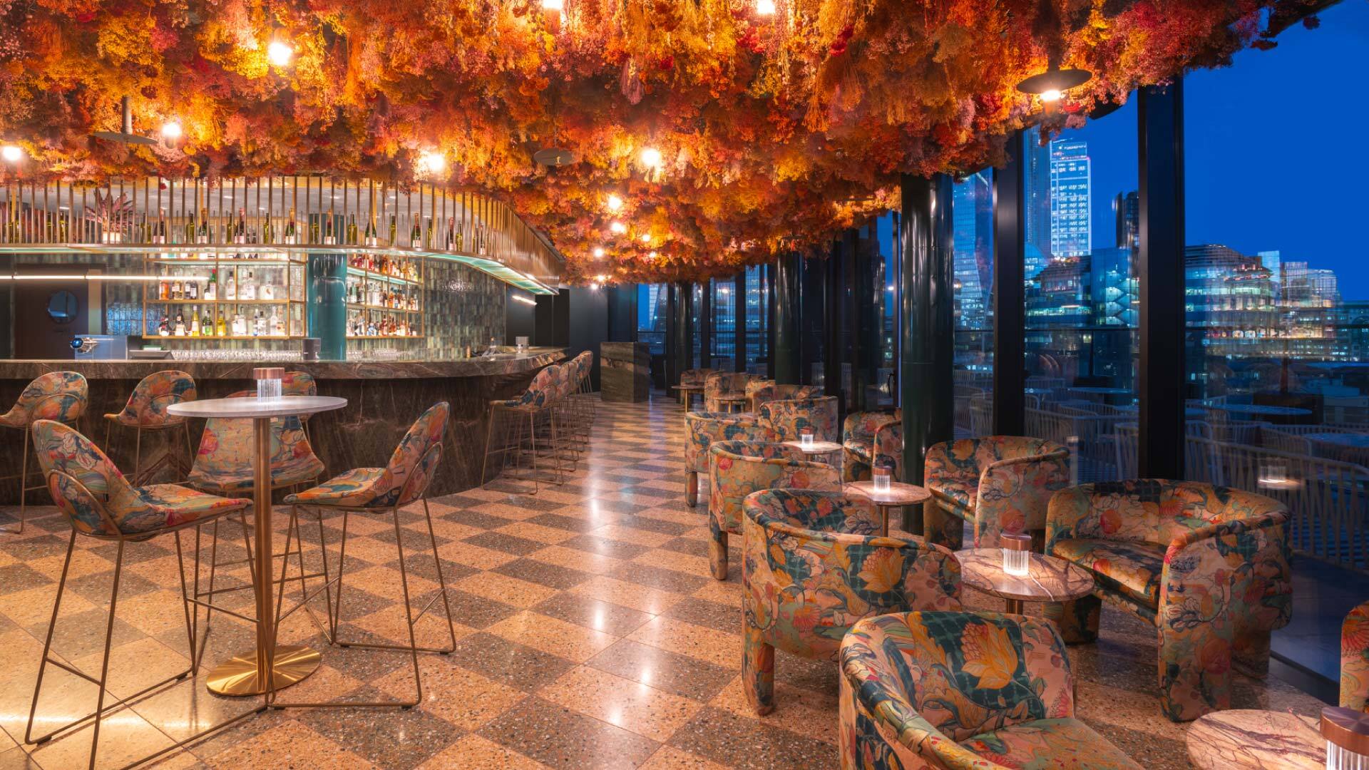 11 Rooftop Bars & Restaurants in the City of London - Florattica at Canopy by Hilton - corner bar, with lounge and high seating, dense flowers hang from the ceiling