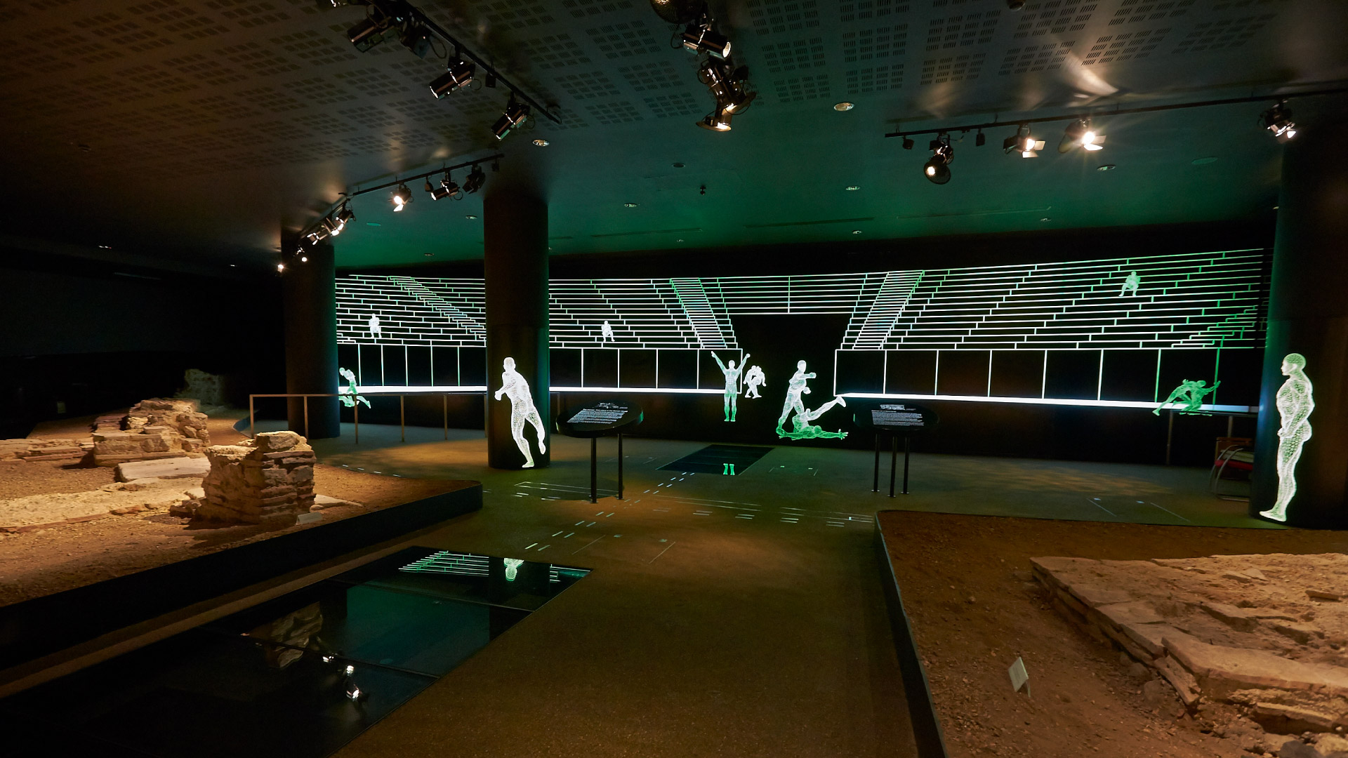 Family Fun Activities to Enjoy on the Weekend in the City of London - Roman ruins of an amphitheatre in a dark room with lit figures around the room doing traditionally roman sports actvities