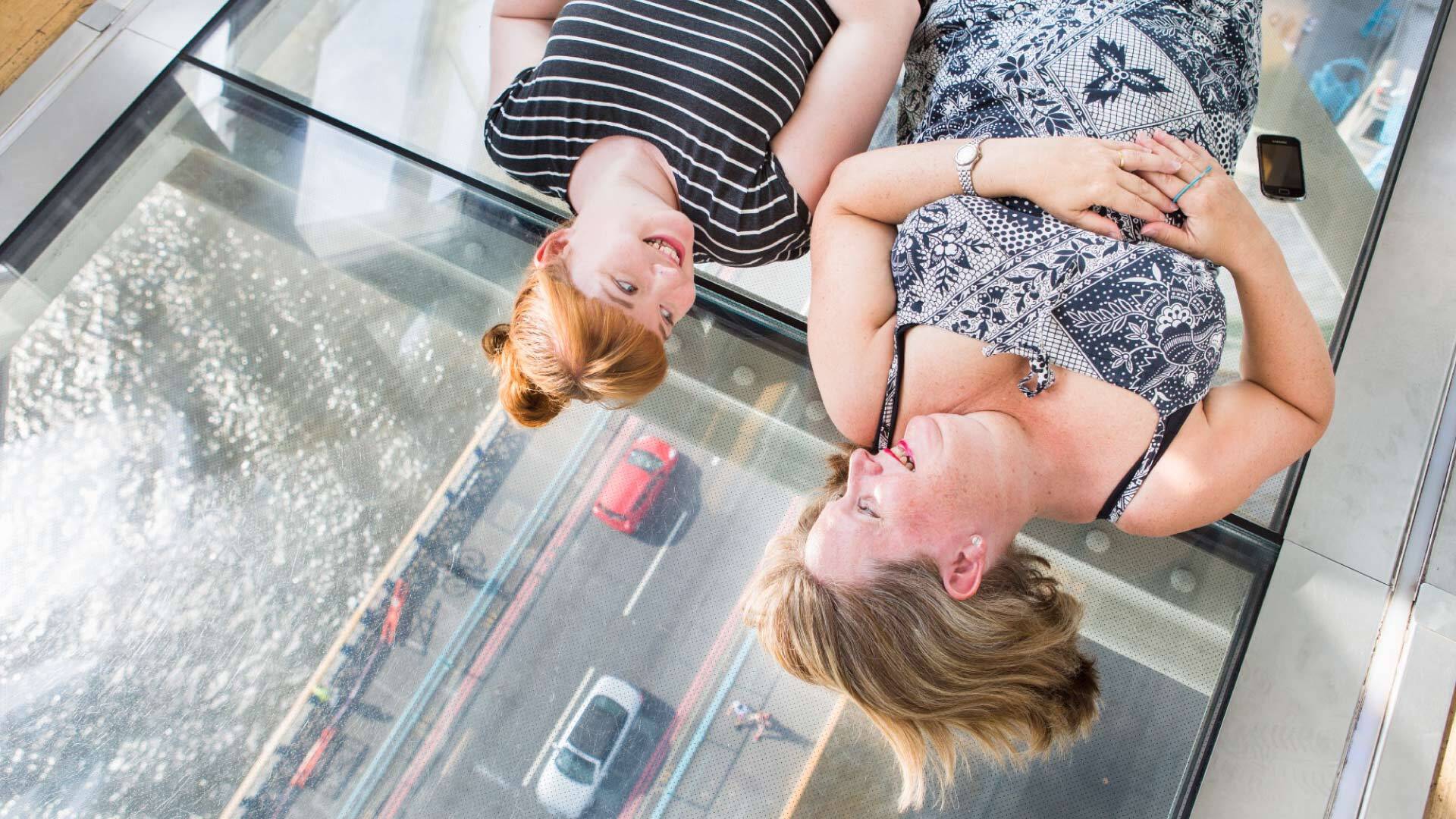 8 best Instagrammable places in London - Glass Floor Tower Bridge - two people lying on glass floor with a view of the Thames below
