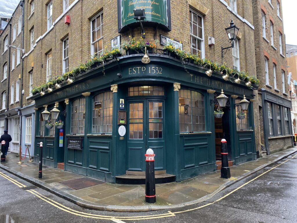 9 Best Pubs in the City of London - The Hand and Shears exterior on the corner of the street, it's dark green with flowers along the top of the building