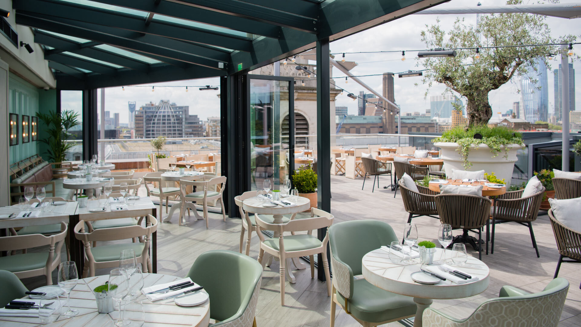 11 Rooftop Bars & Restaurants in the City of London - Vintry & Mercer Hotel - circular tables on roof terrace, large potted olive tree