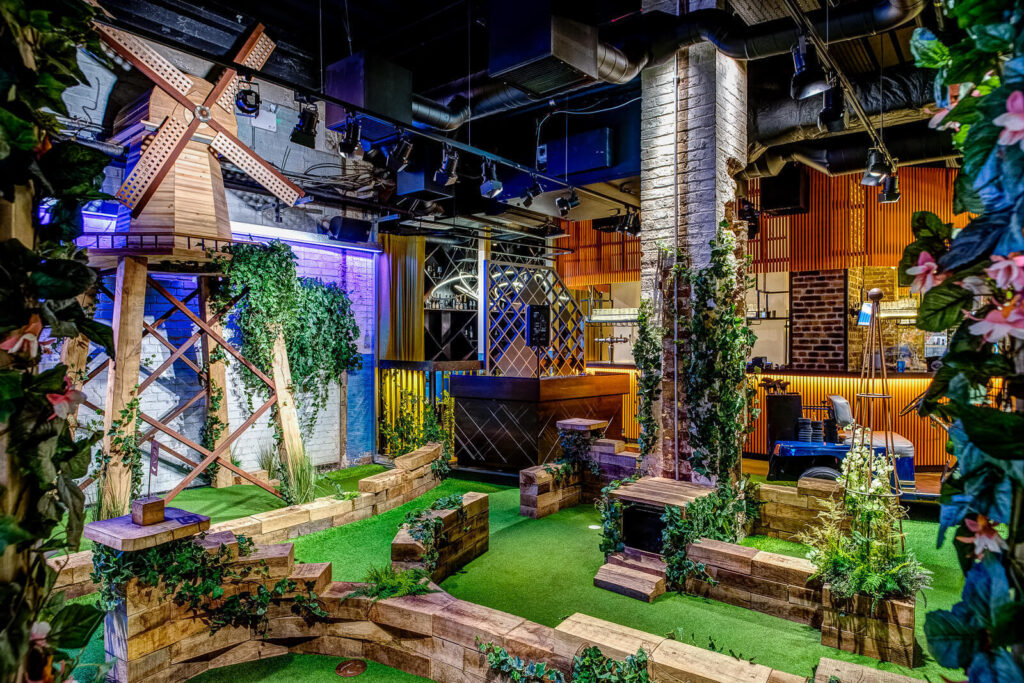 9 Best Brunch Spots in the City of London - Swingers City - indoors crazy golf course, fake ivy running along the course walls and a windmill on a stand in the backgorund 