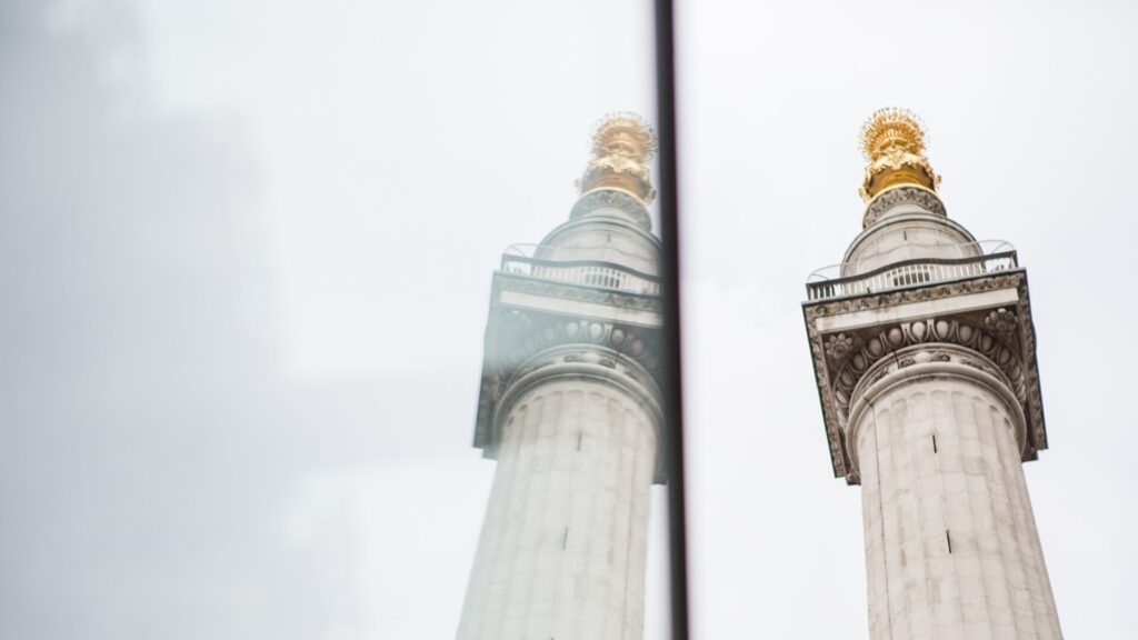 The Monument - a pillar in the reflection of a building with a gold top