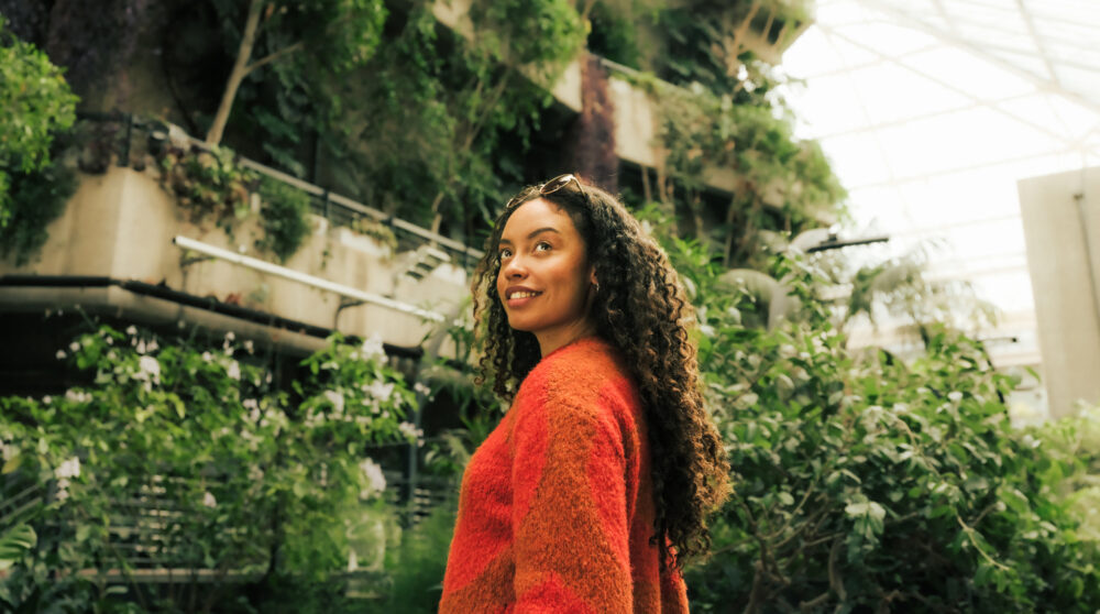 Experience - Woman in Barbican Conservatory - tropical plants flowing over concrete balconies