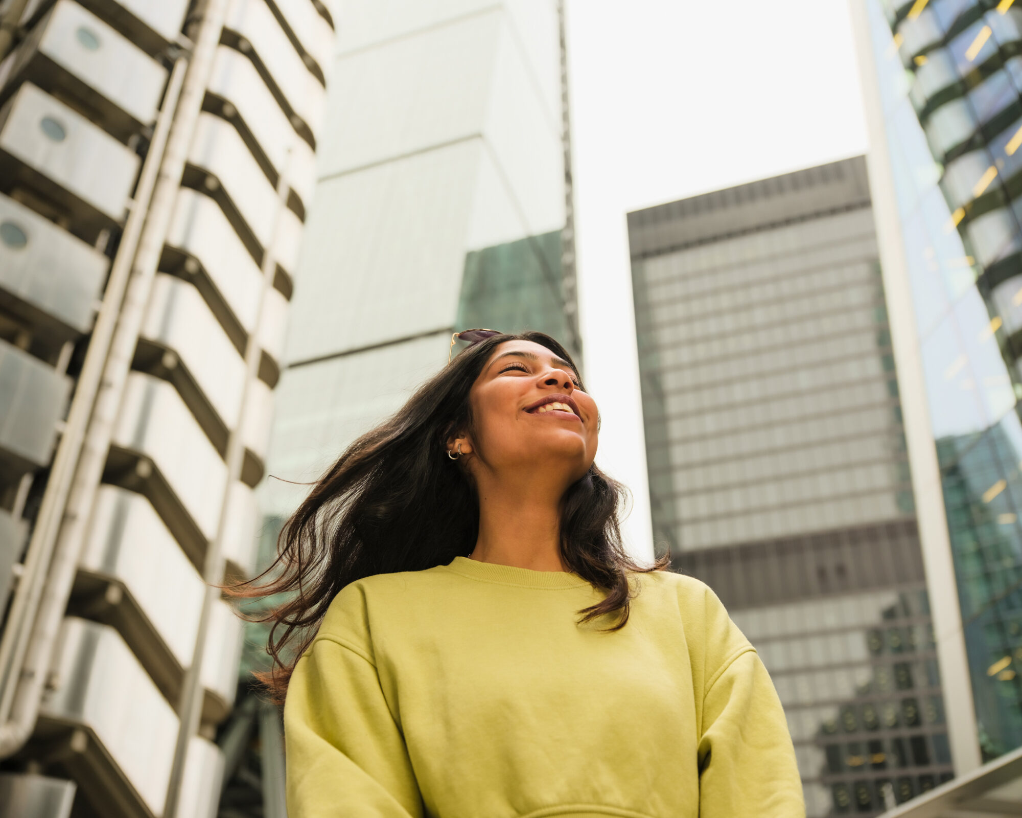 Yoga, Spas and Green Spaces in the City of London - woman smiling in front of Lloyd's building - view looking up towards sky scrapers