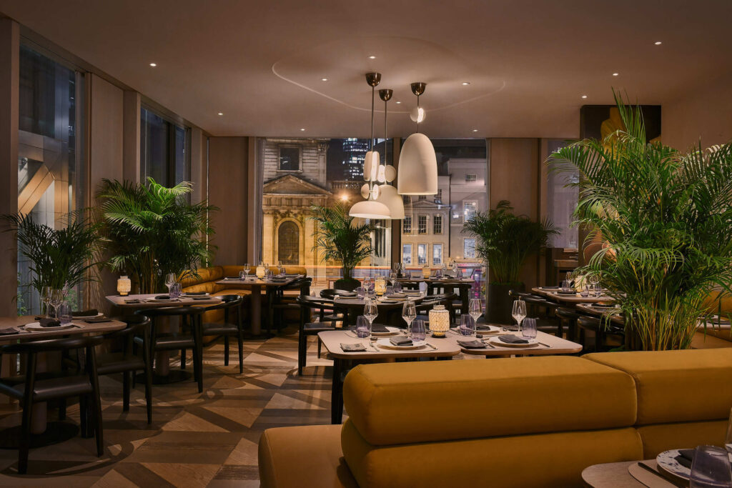 Straits Kitchen - a dimly lit lobby with a yellow sofa and green plants