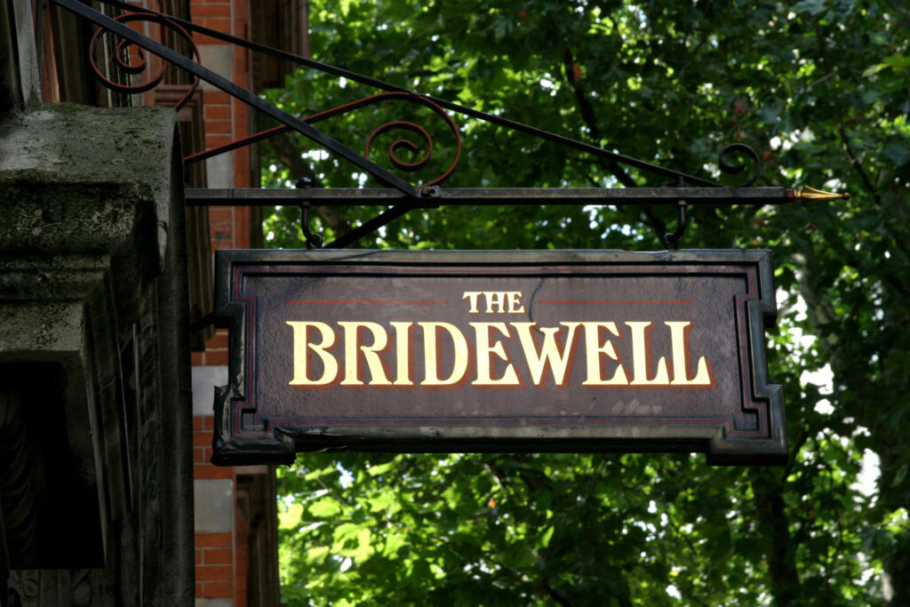 Bridewell Theatre - the sign says the name in old script on a black base with trees in the back ground