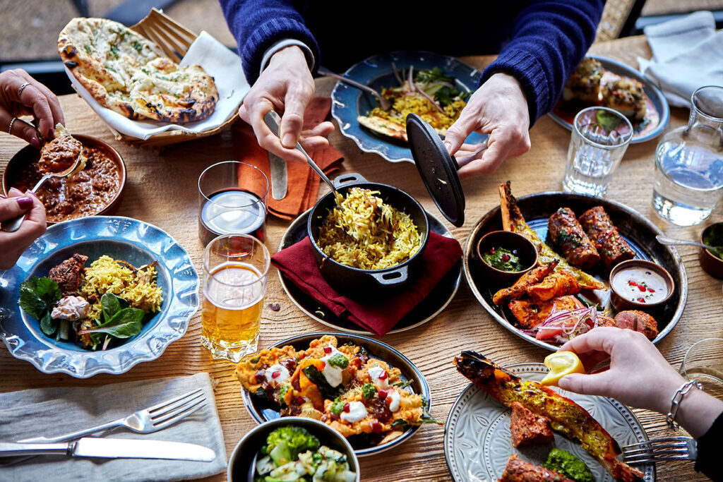 19 best restaurants to eat in the City of London - Cinnamon Kitchen - wooden table with a spread of dishes and drinks, curry and fried snacks