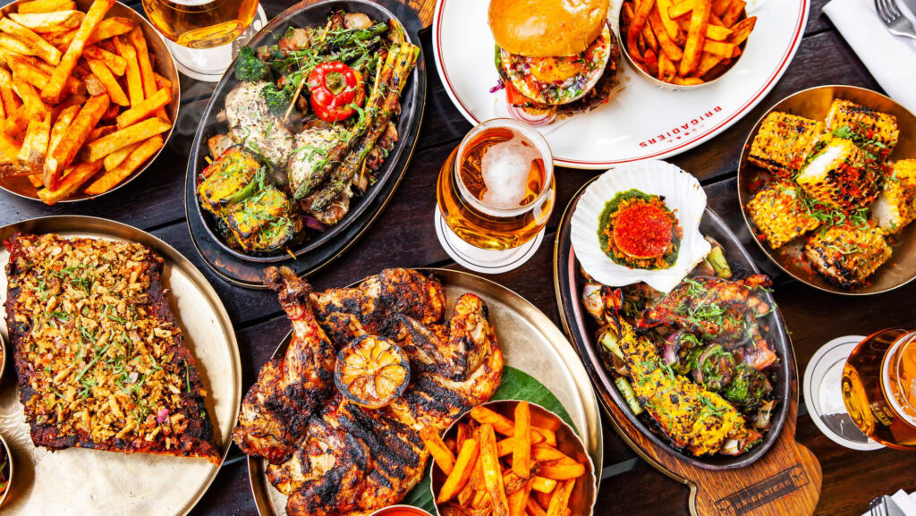 19 best restaurants to eat in the City of London - Brigadiers - table with a spread of dishes and beer, roast chicken, steak, burger, chips and corn