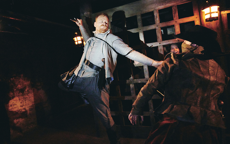 Actors dressed up and performing in front of an audience hiding behind a grid simulating a cage