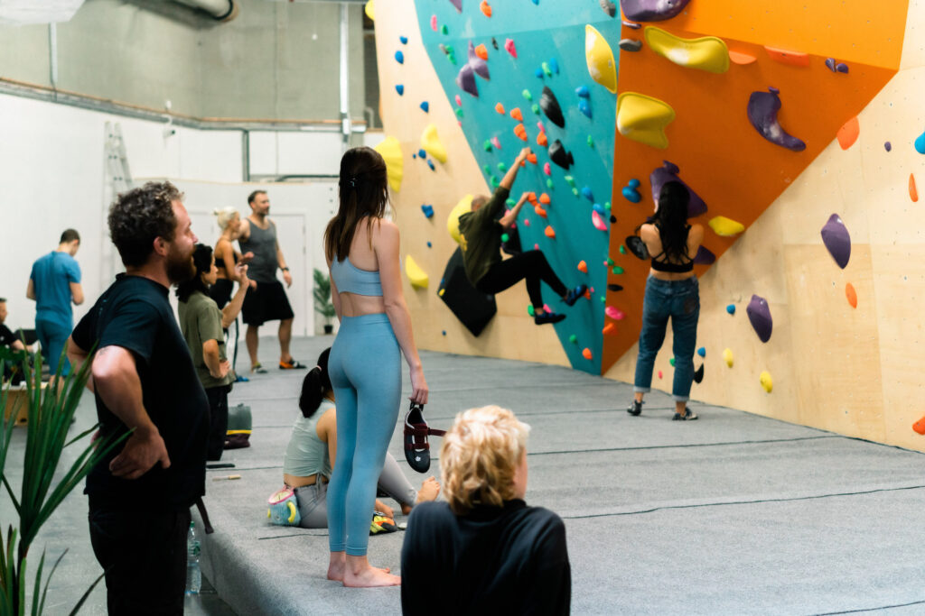 City Bouldering - colourful climbing wall - people watch as others climb the wall - a soft safety matt below