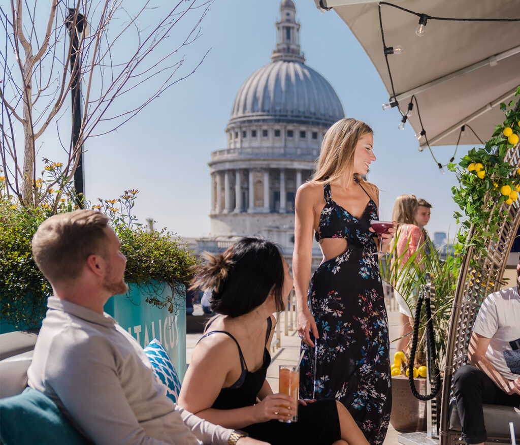 Group of friends having a drink at a rooftop terrace with St Paul's cathedral dome in the background
