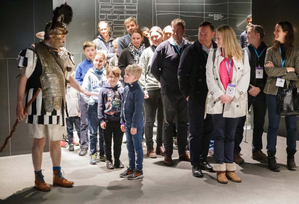 Roman London Family Quest - man wearing roman soldier outfit makes visitors line up - children at the front - parents smiling