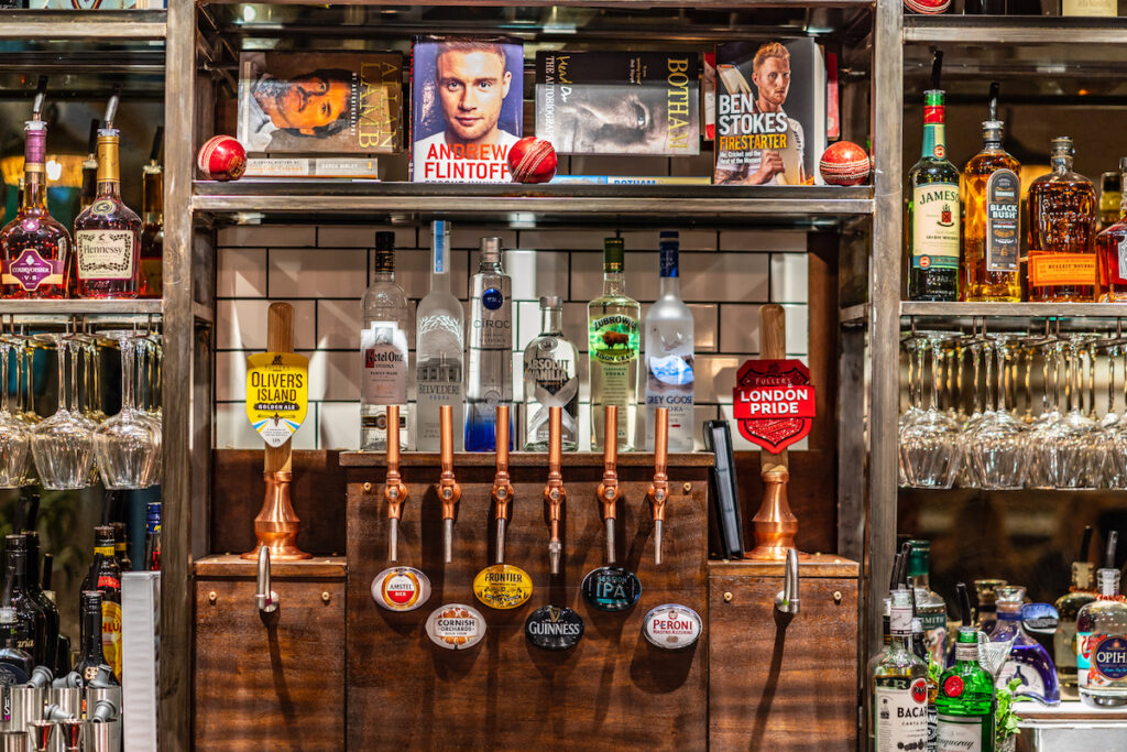 The Pavilion End - view of the bar back - beer taps on the wall - wine glasses - circket balls and cricket books on a shelf