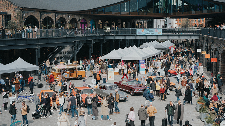 On-street market with clothing stalls, vintage cars and people visiting