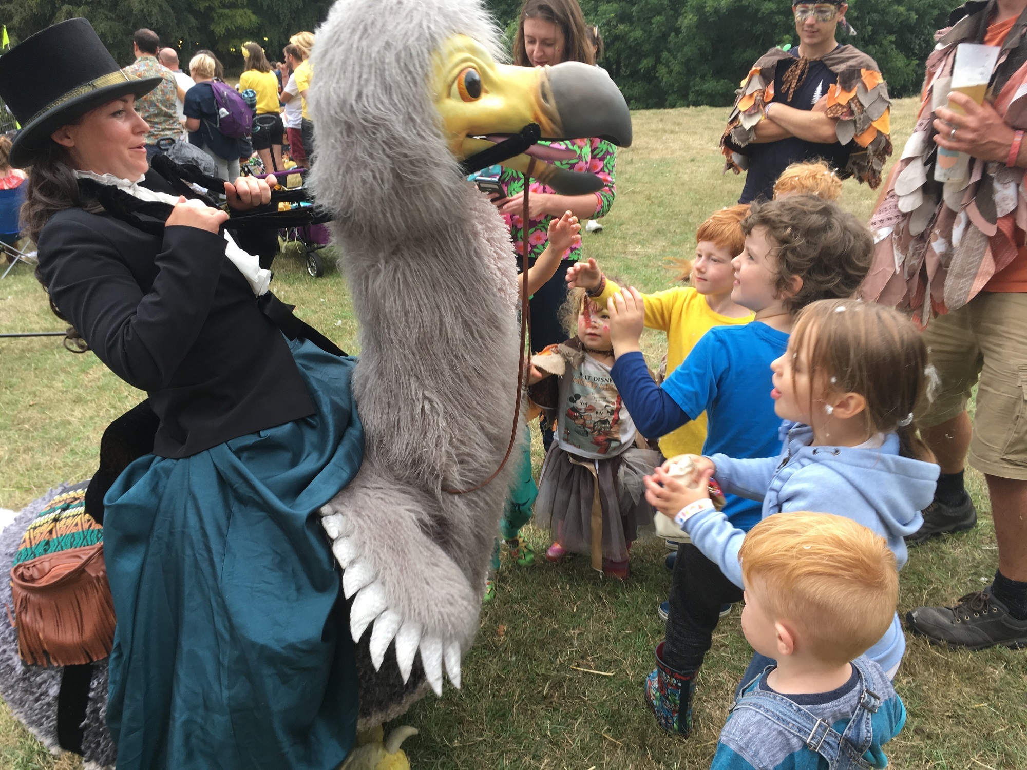 Lady riding a fake life size dodo bird surrounded by children