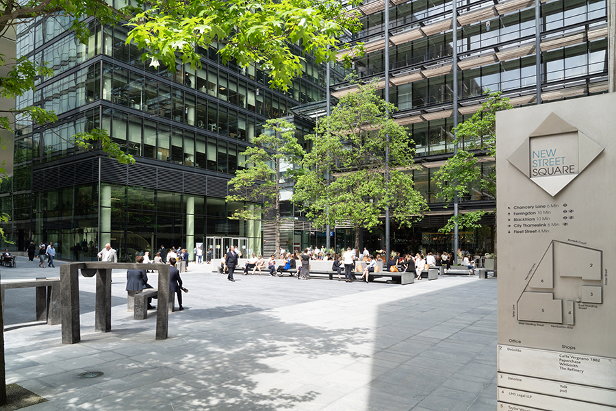 People sitting in line on a bench at a City square surrounded by glass buildings