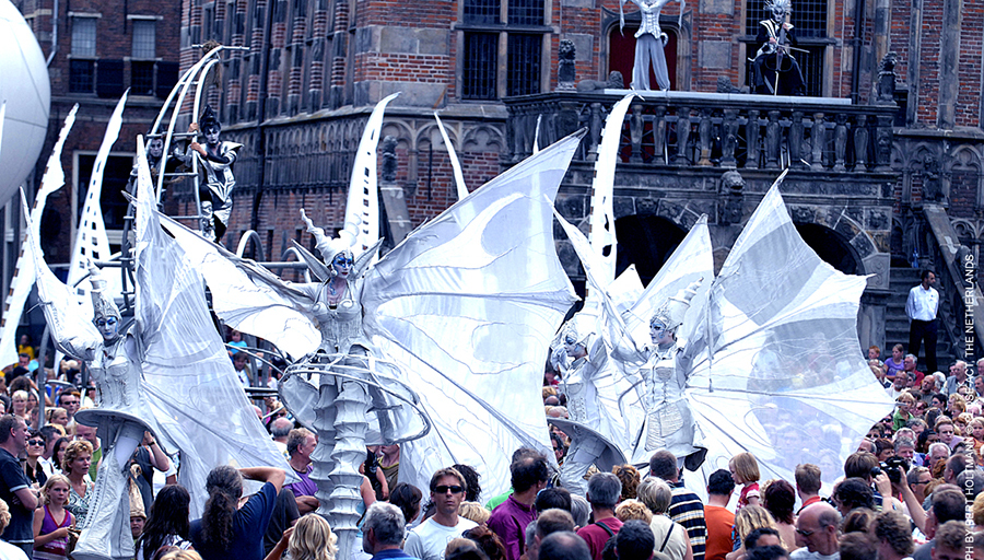 Parade of performers wearing big white wings across the crowds