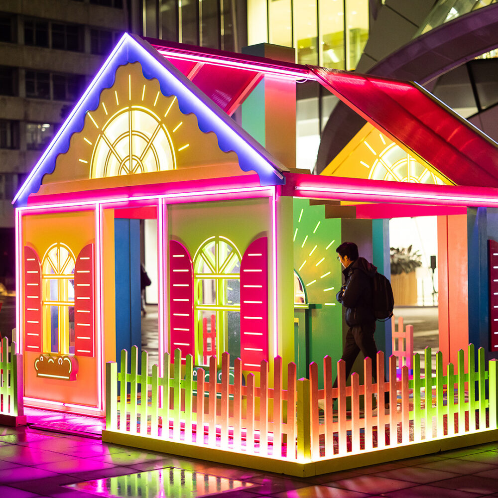 One person entering an immersive light installation in the form of a colourful house