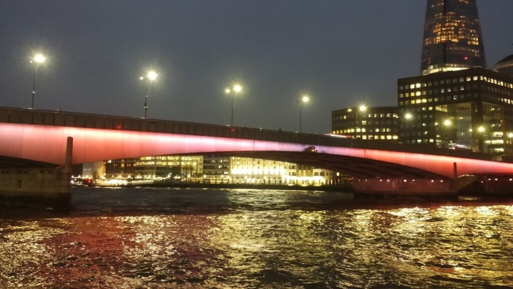 London Bridge illuminated by different coloured lights, reflected back into River Thames.