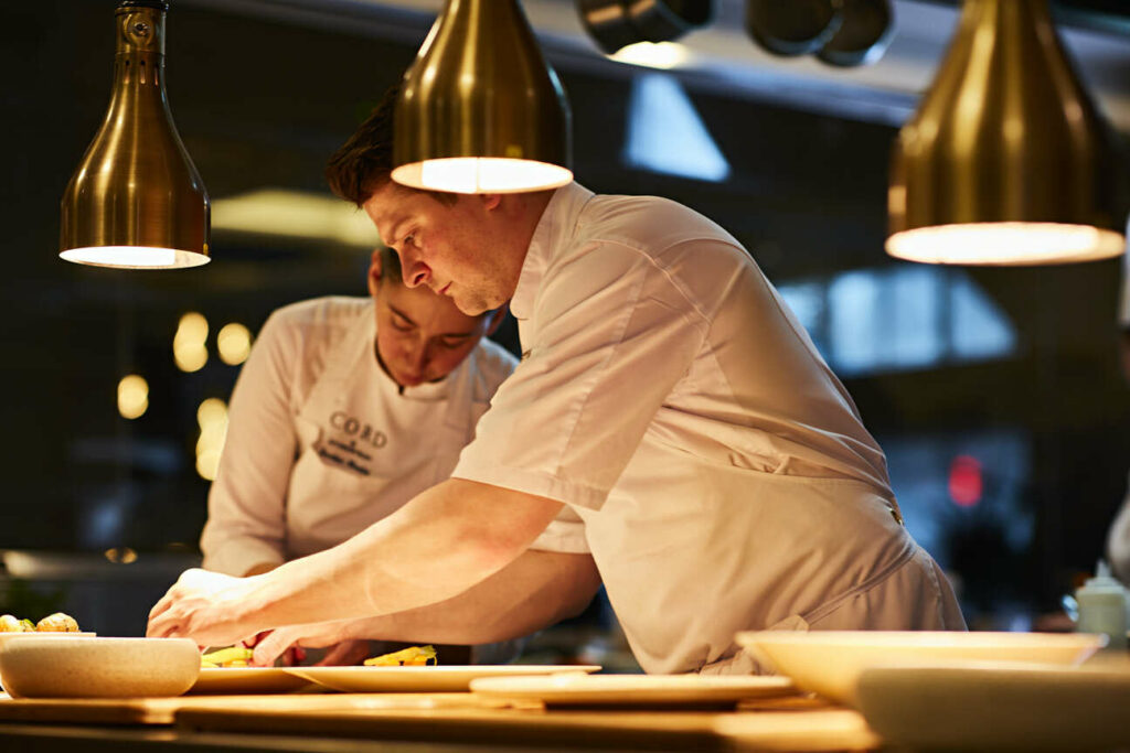 Two chefs plating food in a kitchen.