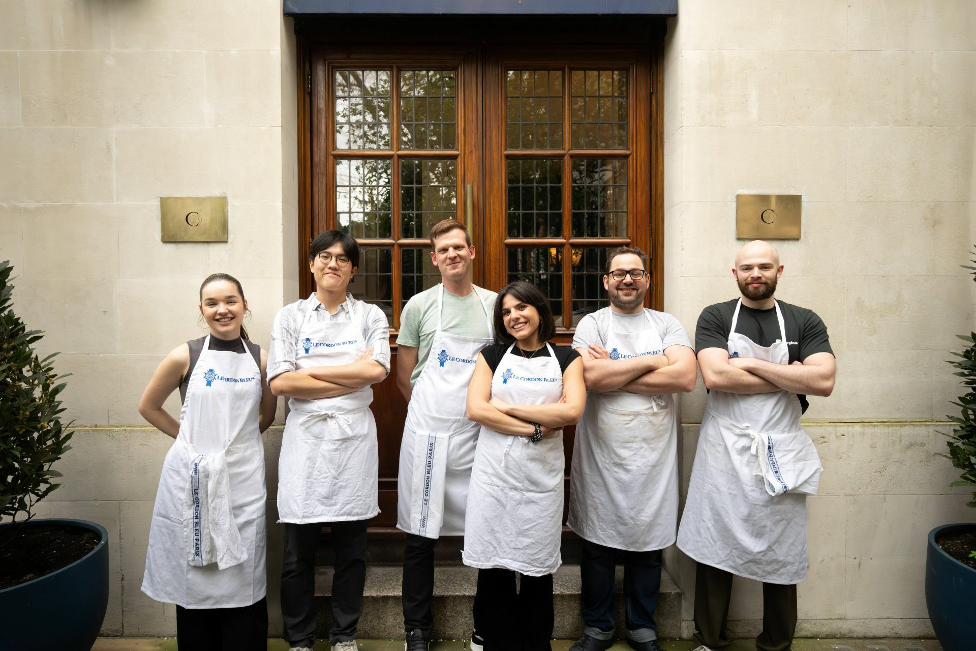 A group of people standing in front of a building, wearing professional kitchen aprons reading "Le Cordon Bleu"
