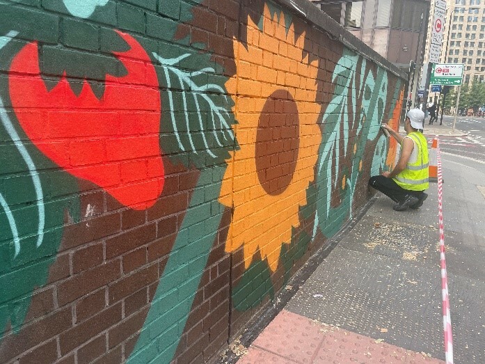 An artist creating a brightly coloured mural on a brick wall.