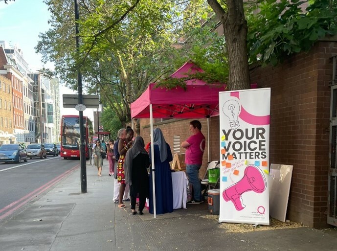 A pop-up banner and stand on a pavement, with people around it,