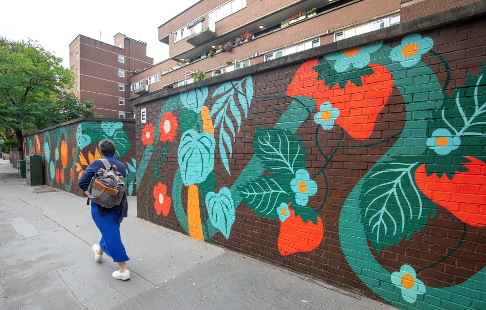 Women walking past a brightly coloured mural featuring plants, flowers, fruits and vegetables.