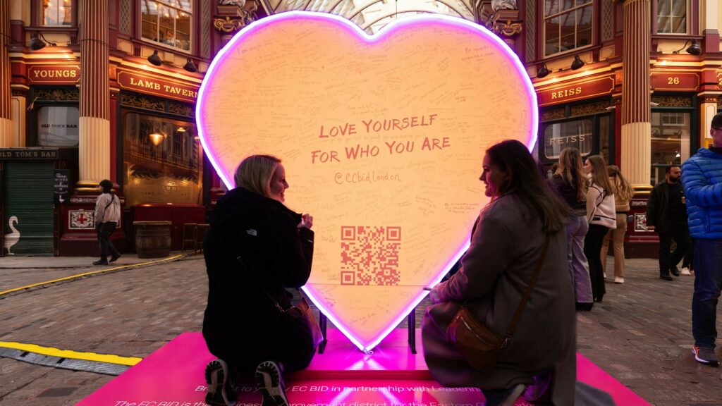 Two people in front of a large light up heart in Leadenhall Market.