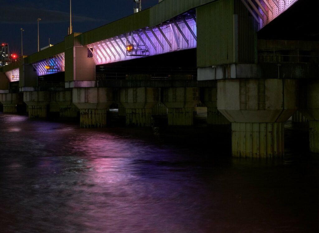 Bridge across River Thames illuminated with purple and pink lights.