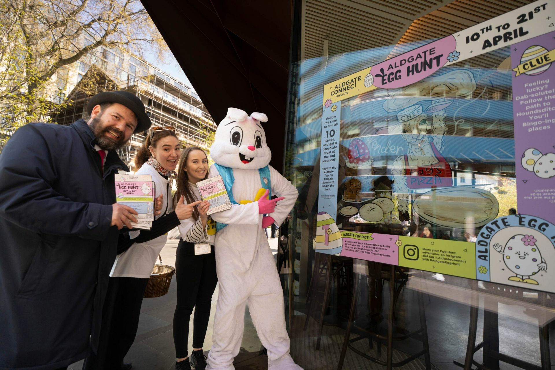Four people, including one in a bunny costume, are posing for an Easter egg hunt promotional poster