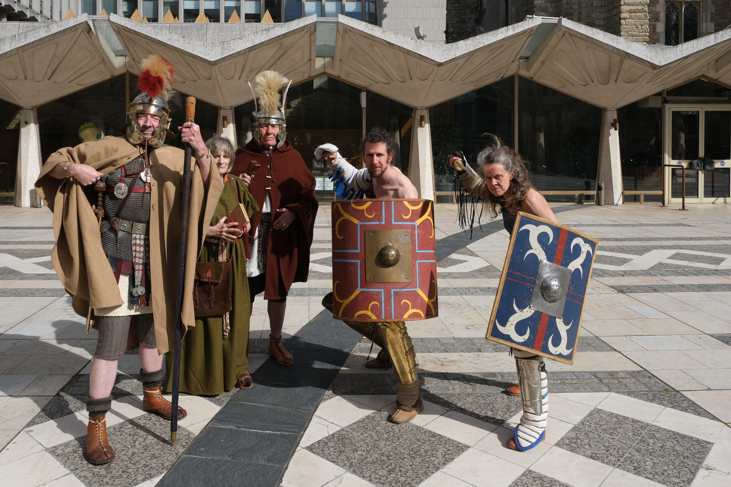 Five people standing in a sunny Guildhall Yard dressed as Roman Gladiators and posing for them camera.