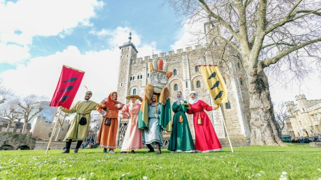 A group of people dressed in medieval costumes holding flags outside the Tower of London.