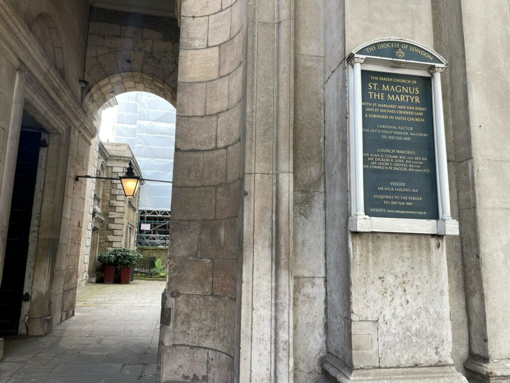 Grey stone exterior of St Magnus the Martyr church. Sign outside of the building with text 'The Parish Church of St. Magnus the Martyr' and information on the cardinal rector, church wardens, verger and enquiries.