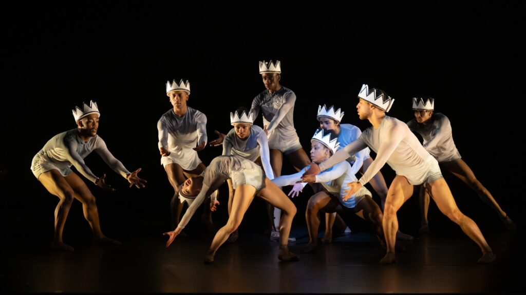 Dancers performing on stage, wearing white crowns.