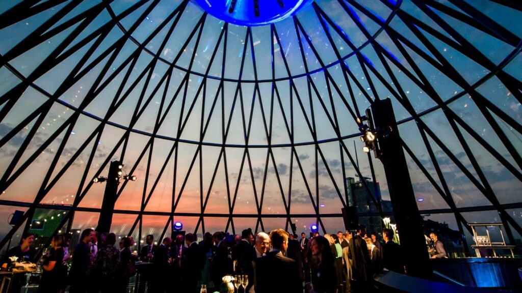 People in a bar with a view of the sunset through the glass roof (the Iris bar at the top of the Gherkin).
