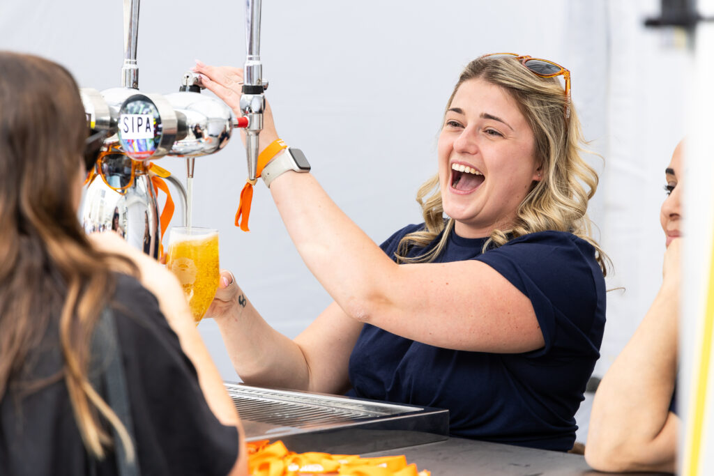A person pulling a pint of beer at City Beerfest smiling and laughing.