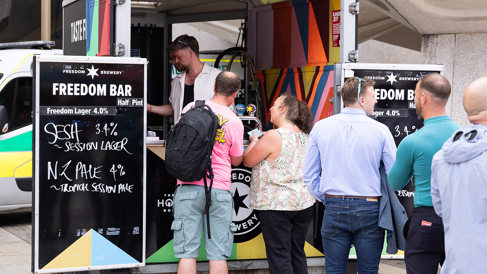 A line of people forms outside a vibrant truck as they wait to purchase beverages.