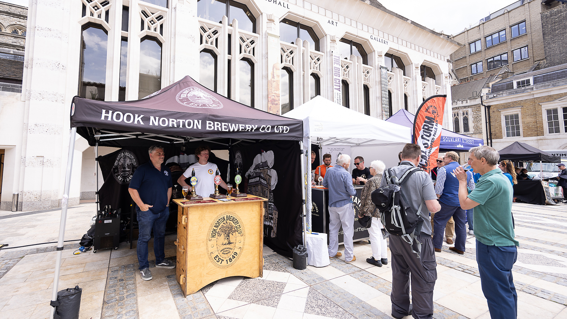 Four stalls at City Beerfest with people ordering food & drinks and standing talking.