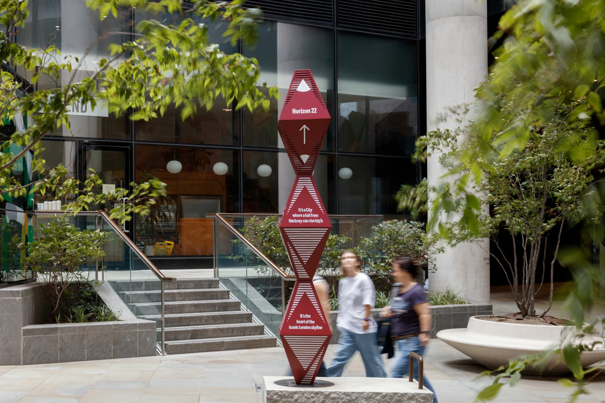 Image of a plinth titled 'City Views' infront of a large glass building with people walking past