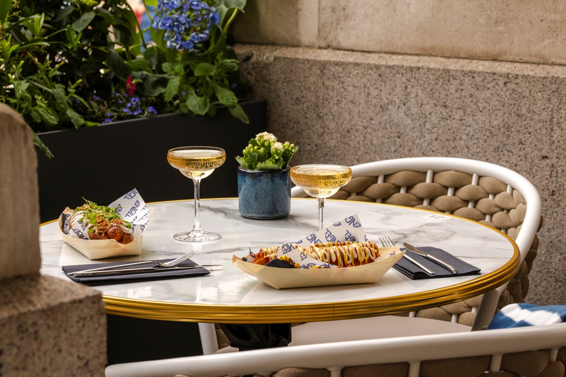 Hot dogs and glasses on champagne on an outdoor table.