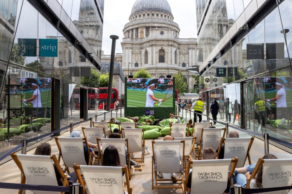 People in deckchairs watching tennis on a big screen, with St Paul's Cathedral in the background.