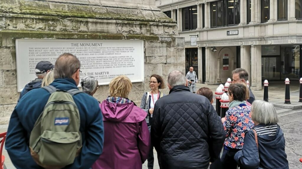 A group of people on a guided tour, listening to a guide in front of the Monument to the Great Fire of London.