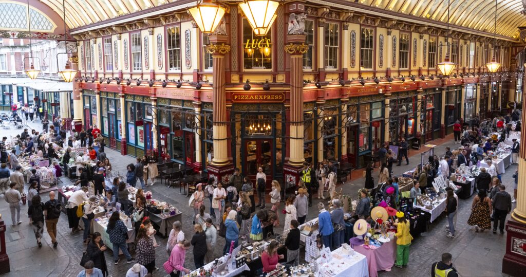 Crowded market fair area at Leadenhall Market, with people browsing long tables in front of the storefronts.