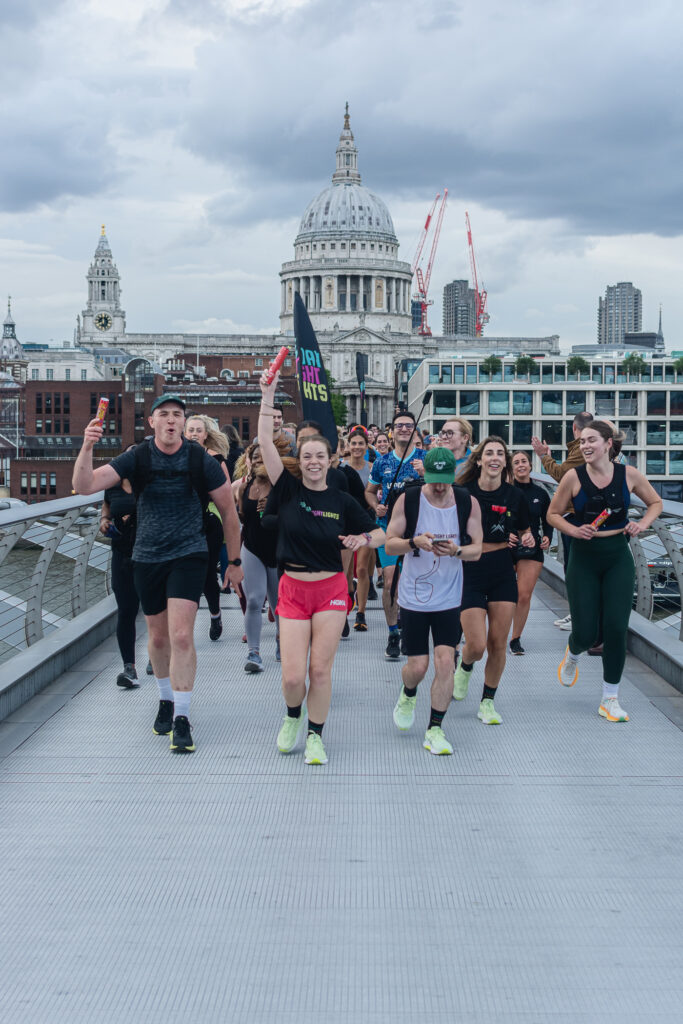 A group of people running over Millennium Bridge in London with St Paul's Cathedral visible in the background.