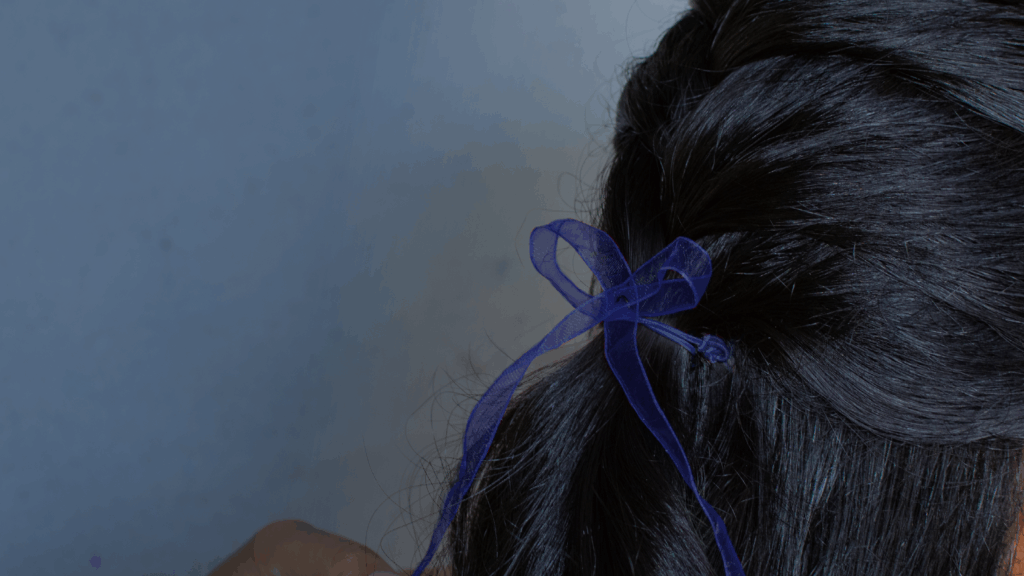 Close-up of the back of a persons head. They have long black hair and a purple ribbon is tied in it.