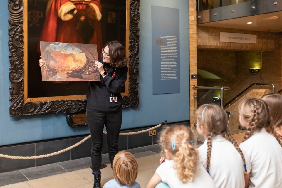 An adult is telling a story to a group of children, within an art gallery
