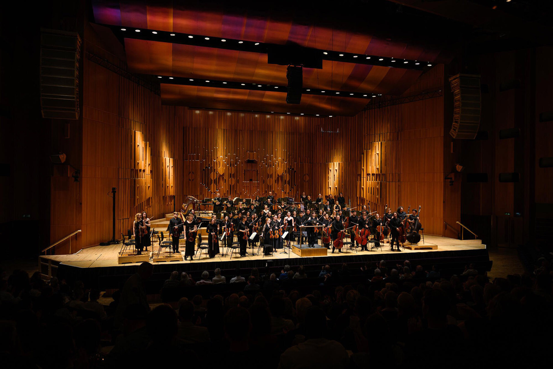 An orchestra performing on stage under warm lighting at a concert hall.