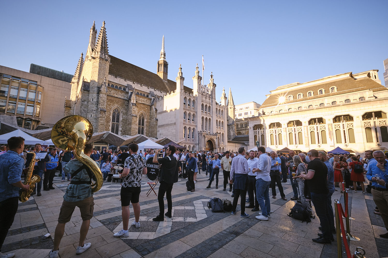 People drinking beer at an outdoor festival in Guildhall Yard. A brass band is playing.